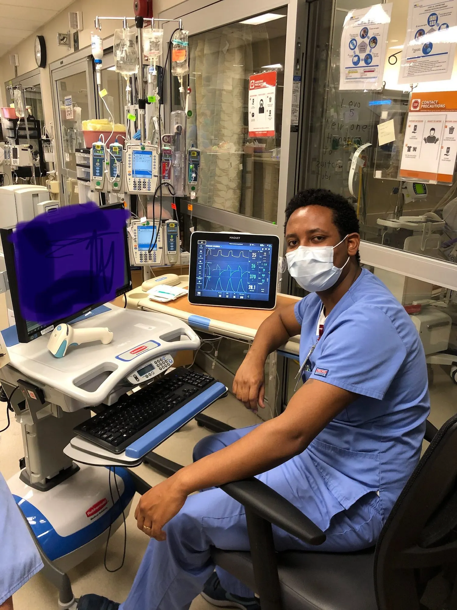 A masked nurse seated at a hospital workstation